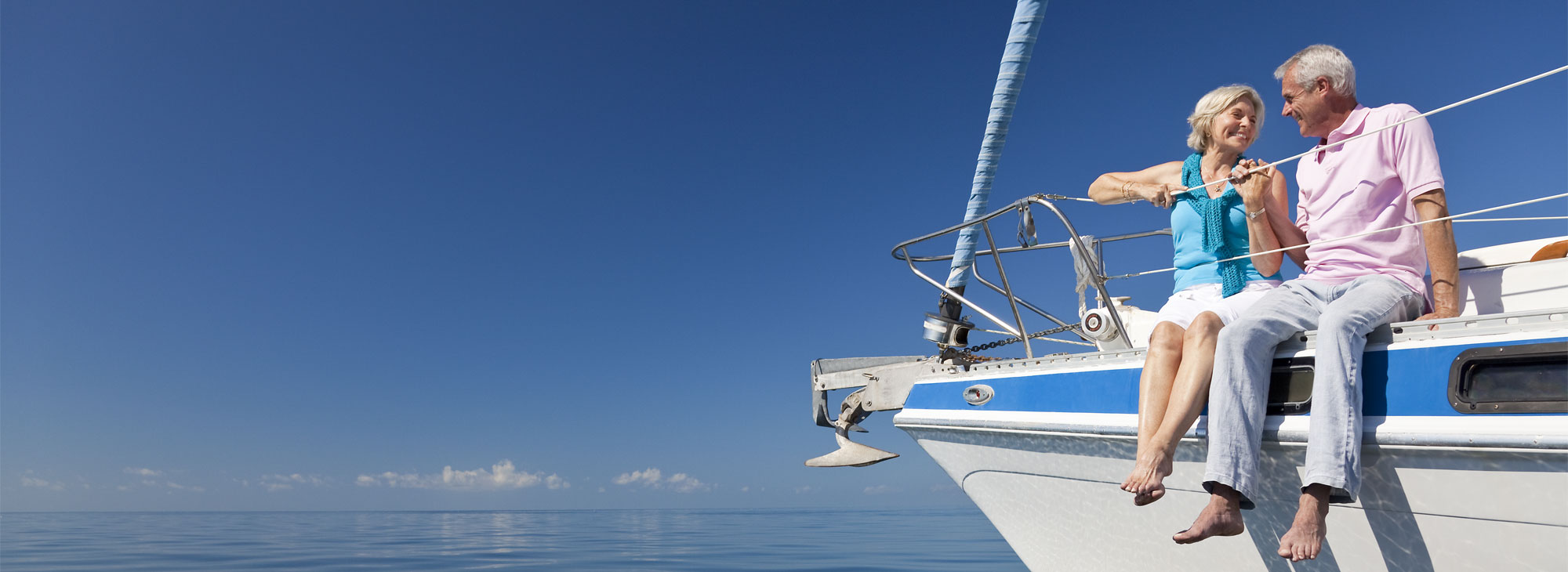 A happy senior couple sitting on the front of a sail boat on a calm blue sea