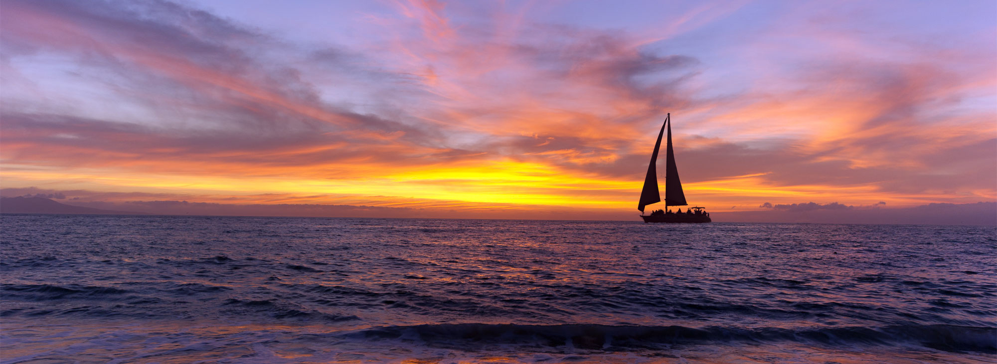 Sailboat sunset silhouette is a colorful vibrant orange and yellow cloudscape sunset.